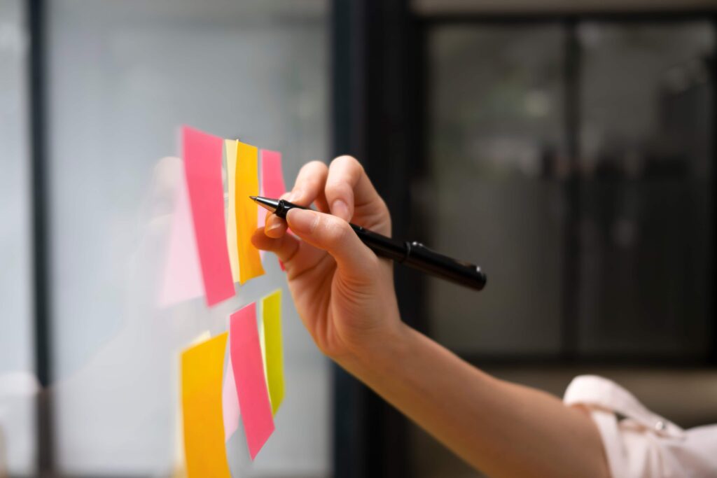 person writing on whiteboard with sticky notes